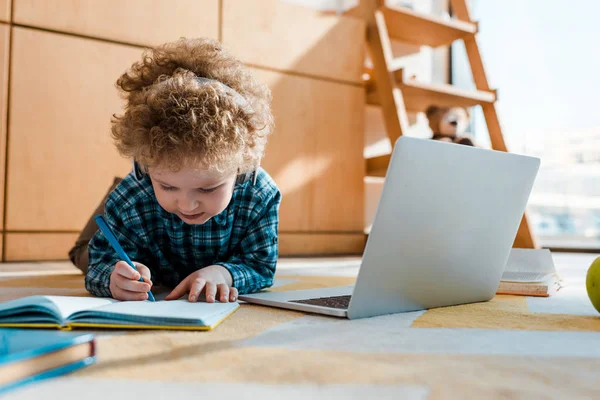 Selective focus of kid listening music in wireless headphones while writing near laptop — Stock Photo