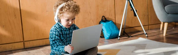 Panoramic shot of happy kid in headphones using laptop — Stock Photo