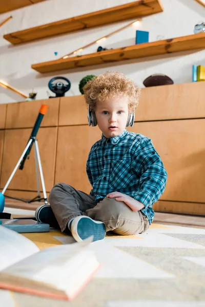 Foyer sélectif d'enfant surpris écouter de la musique dans les écouteurs sans fil tout en étant assis sur le sol — Photo de stock