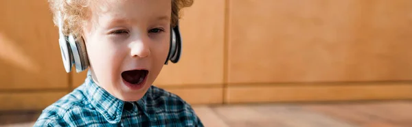 Panoramic shot of tired kid yawning while listening music in wireless headphones — Stock Photo