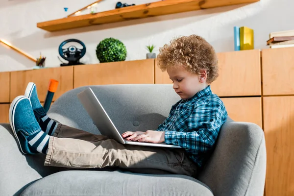 Nettes Kind sitzt im Sessel und benutzt Laptop — Stockfoto