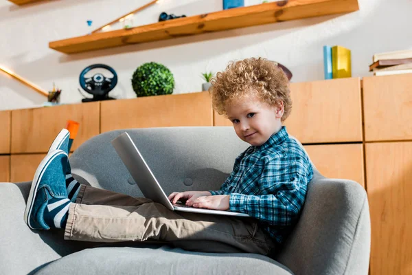 Niño feliz sentado en sillón y el uso de la computadora portátil - foto de stock