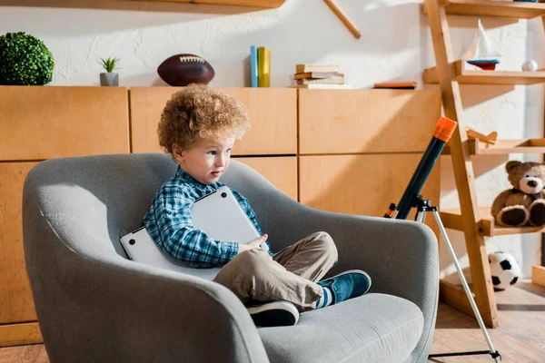 Cute child sitting in armchair with laptop — Stock Photo