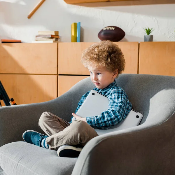 Niño inteligente sentado en sillón con portátil - foto de stock