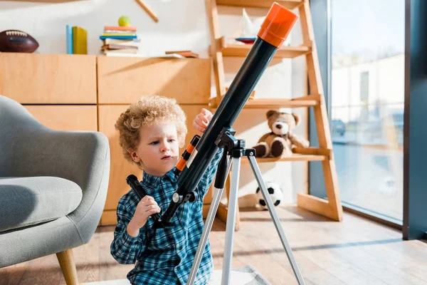 Inteligente niño tocando telescopio cerca de sillón en casa - foto de stock