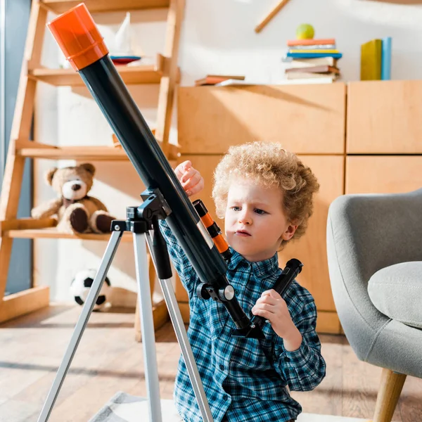 Inteligente niño tocar telescopio cerca de sillón - foto de stock
