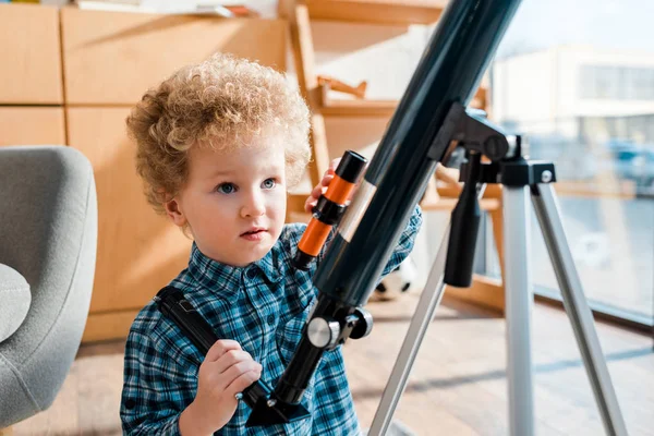 Niño inteligente y rizado mirando el telescopio - foto de stock