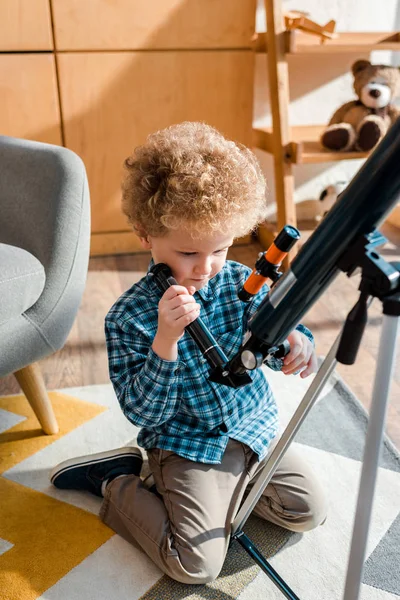 Розумна дитина торкається телескопа, сидячи на килимі — стокове фото