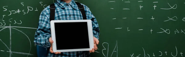 Panoramic shot of smart kid holding digital tablet with blank screen near chalkboard with mathematical formulas — Stock Photo