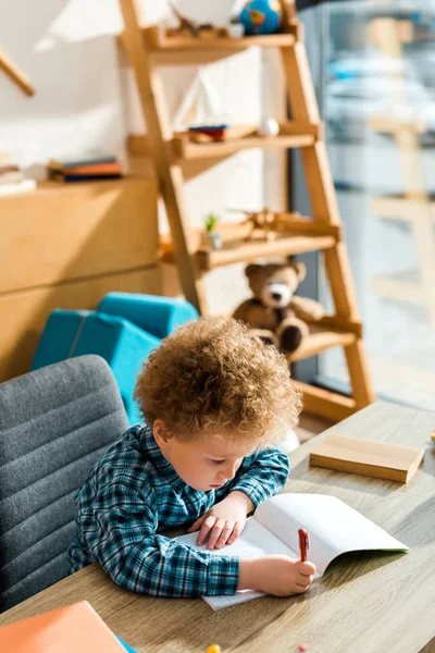 Niño inteligente sentado y escribiendo en el escritorio - foto de stock