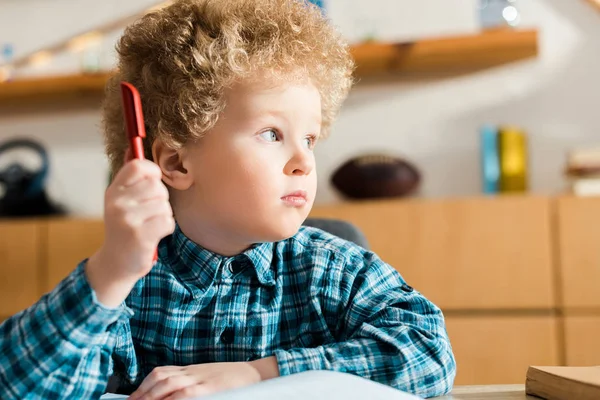 Niño inteligente mirando hacia otro lado y sosteniendo la pluma - foto de stock