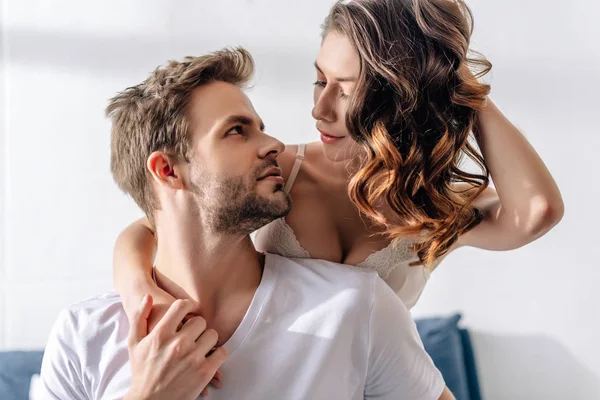 Namorada sexy no sutiã abraçando e olhando para namorado bonito em t-shirt — Fotografia de Stock