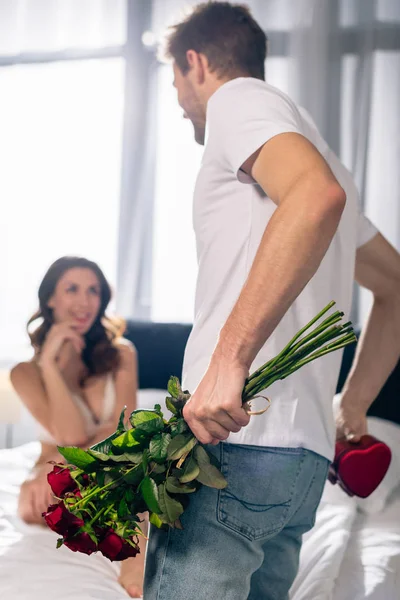 Enfoque selectivo de novio sosteniendo ramo y caja en forma de corazón y novia sonriente mirándolo en 14 febrero - foto de stock