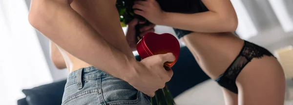 Tiro panorâmico de namorado dando buquê e caixa em forma de coração para namorada sexy em 14 de fevereiro — Fotografia de Stock