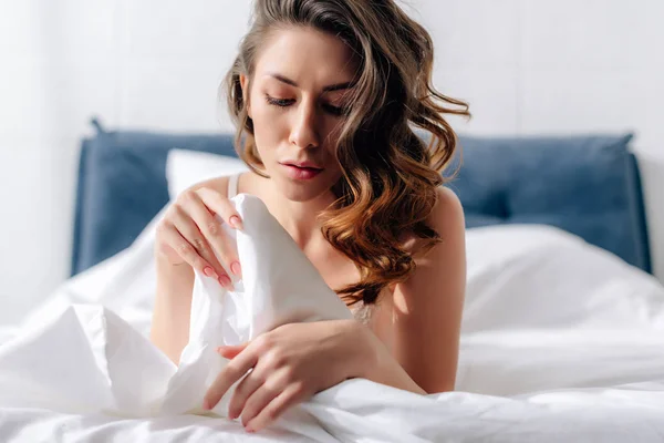 Attractive woman holding blanket and lying in bed — Stock Photo