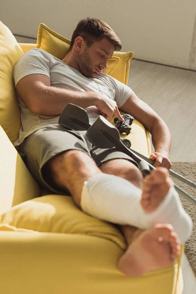 KYIV, UKRAINE - 21 JANVIER 2020 : Beau homme avec jambe cassée dormant près du joystick et béquilles sur le canapé — Photo de stock