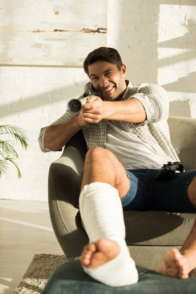 KYIV, UKRAINE - JANUARY 21, 2020: Selective focus of smiling man with broken leg holding crutch and looking at camera at home — Stock Photo