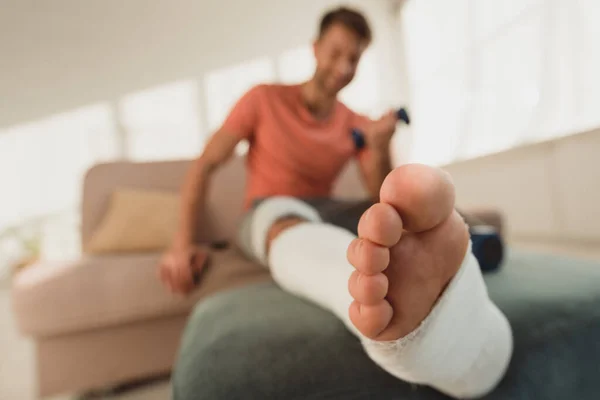 Selective focus of broken leg of man with dumbbell on couch — Stock Photo