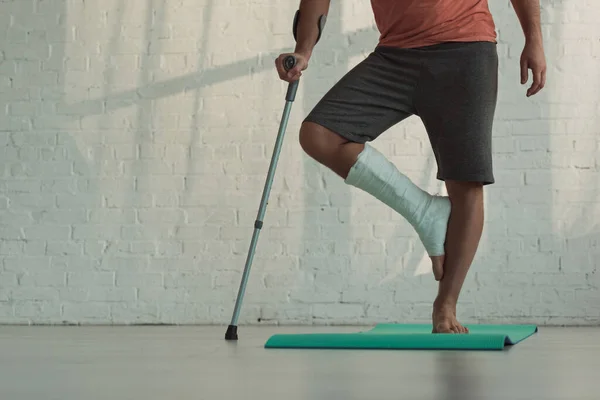 Cropped view of man with broken leg standing on fitness man and holding crutch — Stock Photo