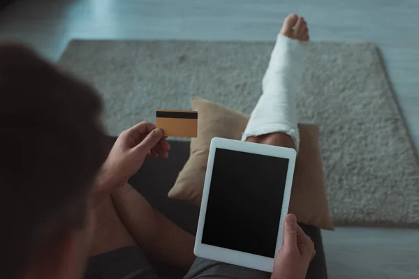 Селективный фокус человека со сломанной ногой, держащего цифровой планшет и кредитную карту — стоковое фото