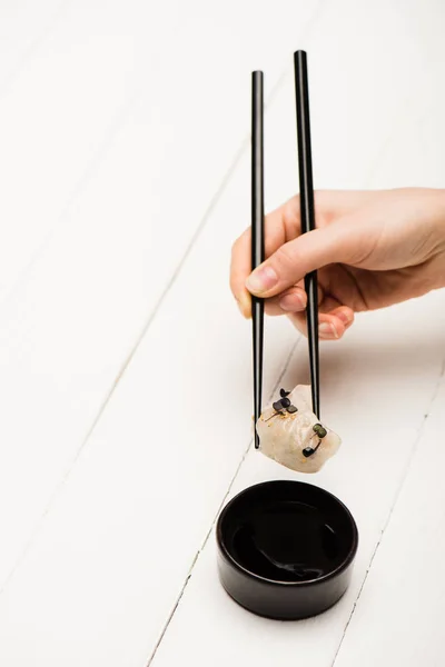 Vista recortada de la mujer comiendo deliciosa bola de masa hervida china con palillos y salsa de soja en la mesa de madera blanca - foto de stock