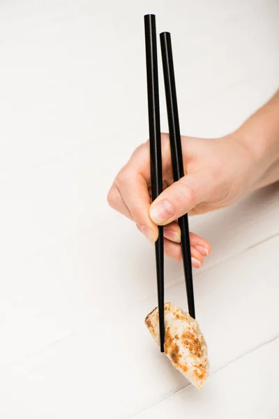 Vue recadrée de femme mangeant de délicieux gyoza avec des baguettes à la table en bois blanc — Photo de stock