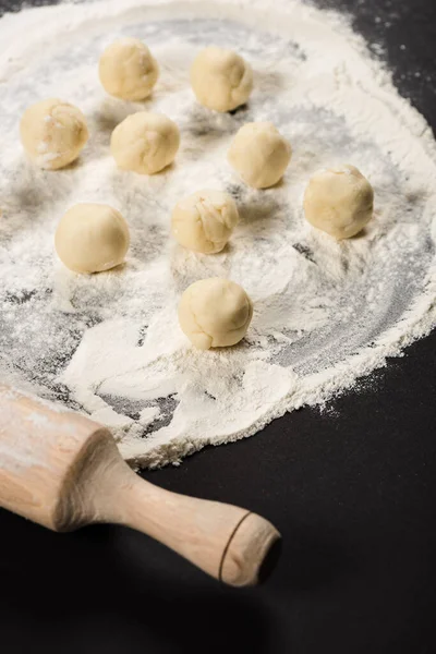 Rohe Teigbällchen für Knödel auf Mehl nahe Nudelholz auf schwarzem Hintergrund — Stockfoto