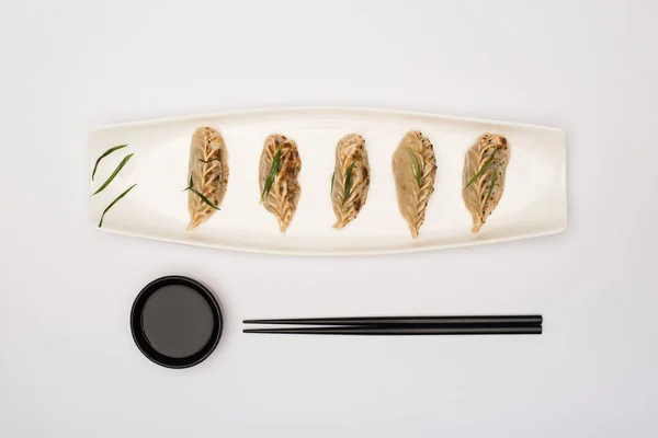 Vue du dessus de délicieux gyoza sur assiette près de baguettes et sauce soja sur fond blanc — Photo de stock