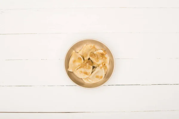 Vista superior de la deliciosa varenyky con cebolla frita en un tazón sobre una mesa de madera blanca - foto de stock