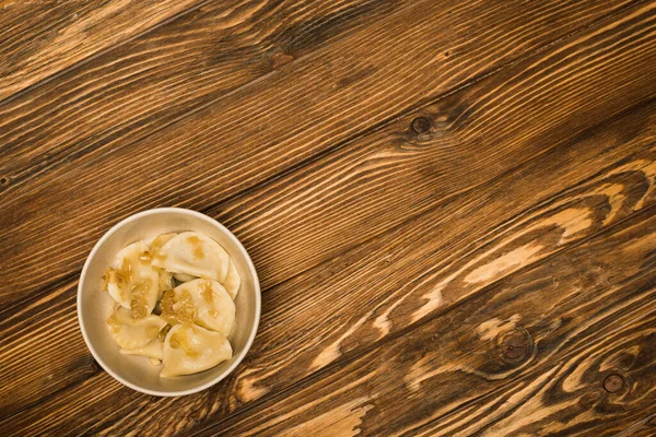 Vista superior de delicioso varenyky com cebola frita na tigela na mesa de madeira — Fotografia de Stock