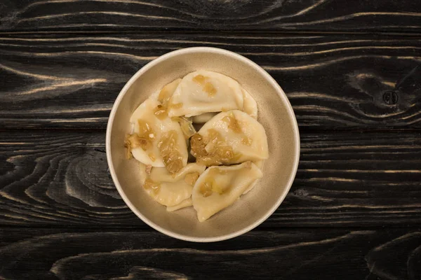 Вид сверху на вкусного вареника с жареным луком в миске на черном деревянном столе — стоковое фото
