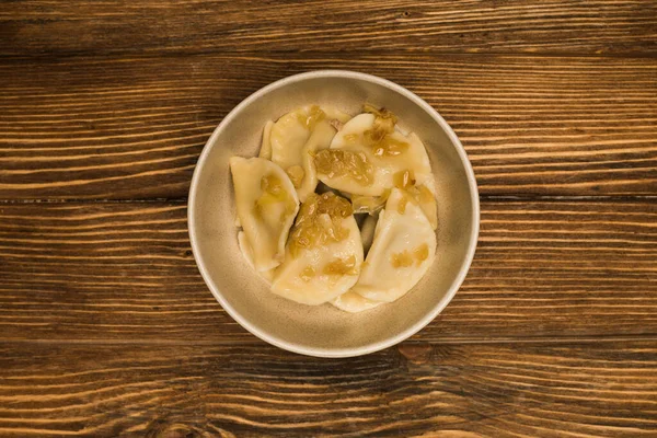 Вид сверху на вкусного вареника с жареным луком в миске на деревянном столе — стоковое фото