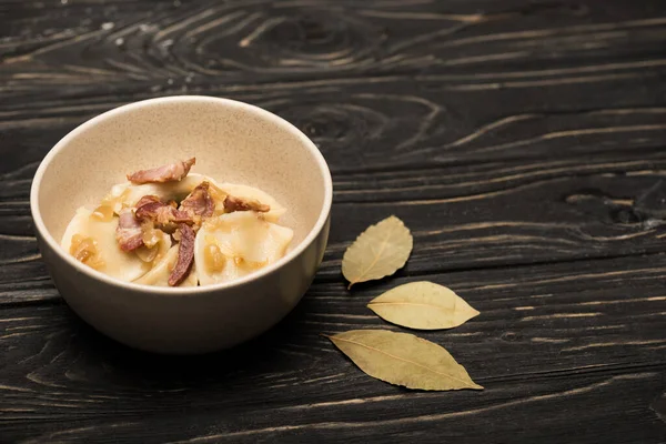 Délicieux varenyky avec craquelins dans un bol près de feuilles de laurier sur table en bois noir — Photo de stock