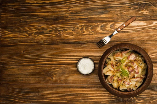 Top view of delicious varenyky with cracklings in bowl served with sour cream on wooden table — Stock Photo