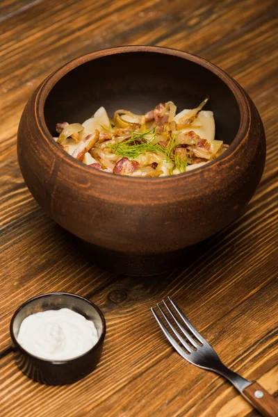 Delicious varenyky with cracklings in bowl served with sour cream on wooden table — Stock Photo