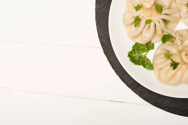 Vue de dessus de délicieux Khinkali avec coriandre sur plaque sur table en bois blanc — Photo de stock