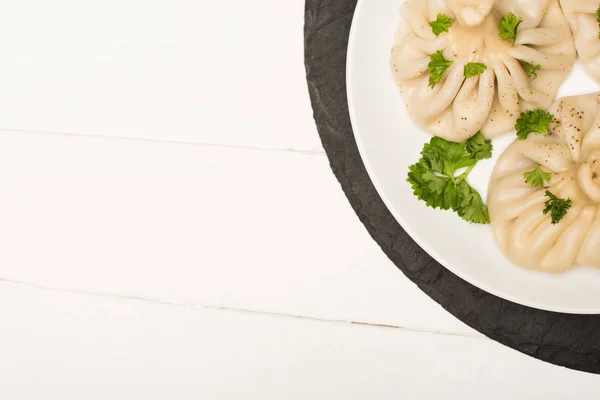 Вид сверху на вкусный хинкали с кинзой на тарелке на белом деревянном столе — стоковое фото