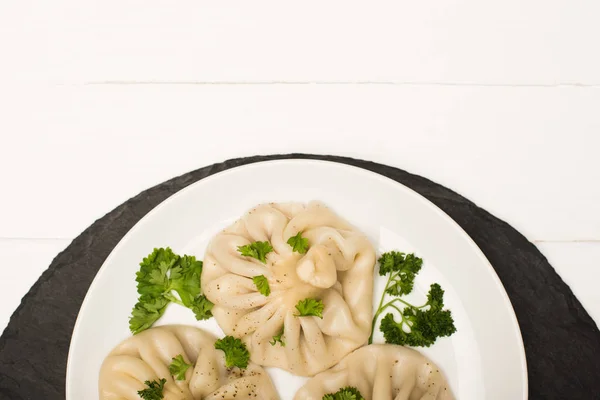 Draufsicht auf köstliches Chinkali mit Koriander auf Teller auf weißem Holztisch — Stockfoto