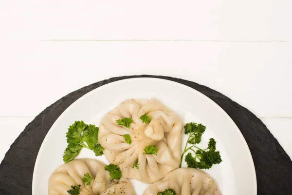 Vista superior de la deliciosa Khinkali con cilantro en plato sobre mesa de madera blanca - foto de stock