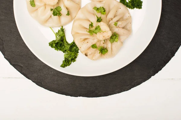 Vista superior de la deliciosa Khinkali con cilantro en plato sobre mesa de madera blanca - foto de stock