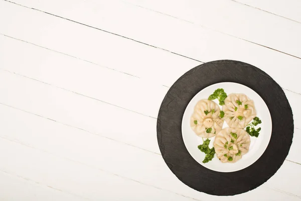 Top view of delicious Khinkali with cilantro on plate on white wooden table — Stock Photo