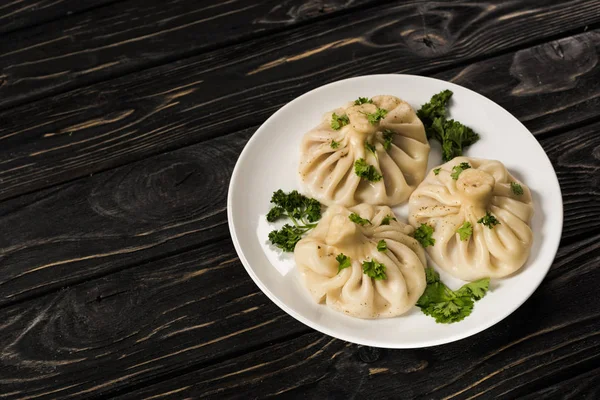 Leckeres Khinkali mit Koriander auf Teller auf schwarzem Holztisch — Stockfoto