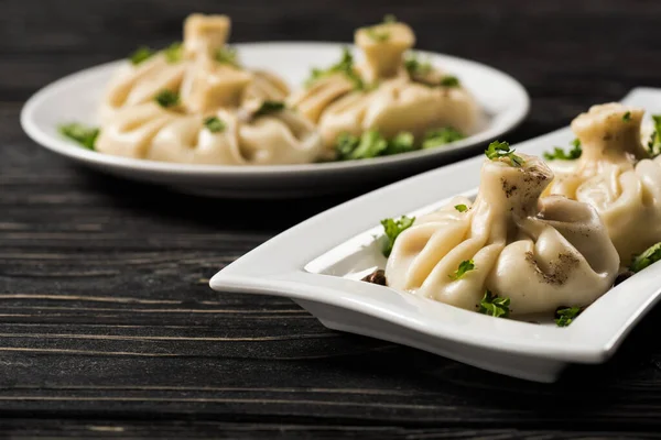 Selective focus of delicious Khinkali with cilantro on plates on black wooden table — Stock Photo