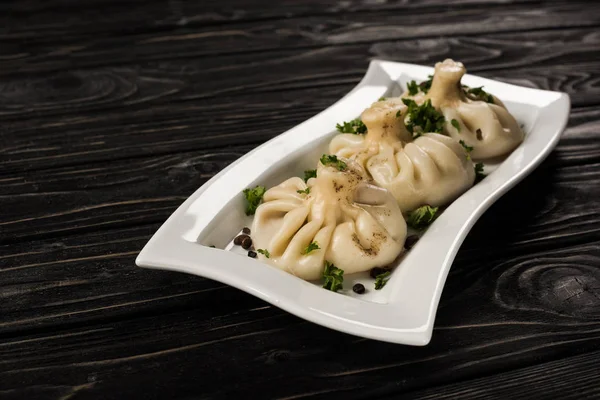 Delicious Khinkali with cilantro on plate on black wooden table — Stock Photo