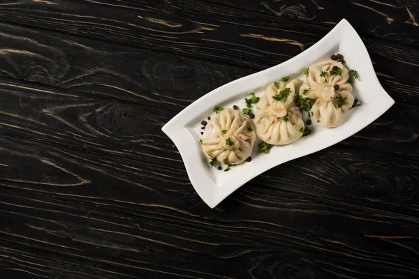 Draufsicht auf köstliches Chinkali mit Koriander auf Teller auf schwarzem Holztisch — Stockfoto