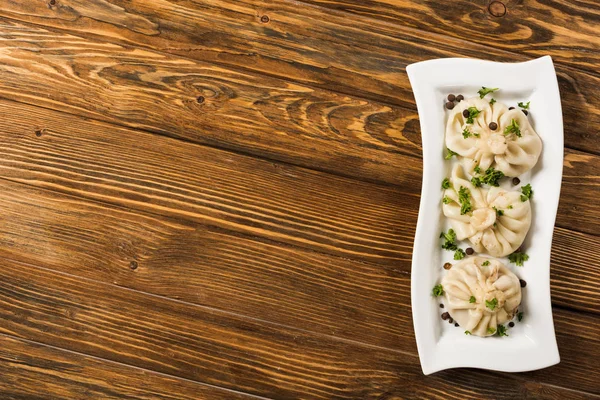 Draufsicht auf köstliches Chinkali mit Koriander auf Teller auf braunem Holztisch — Stockfoto