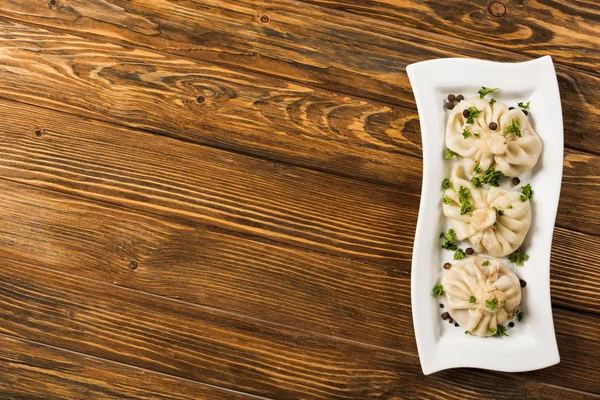 Vista superior de la deliciosa Khinkali con cilantro en plato sobre mesa de madera marrón — Stock Photo