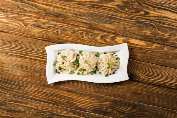 Draufsicht auf köstliches Chinkali mit Koriander auf Teller auf braunem Holztisch — Stockfoto