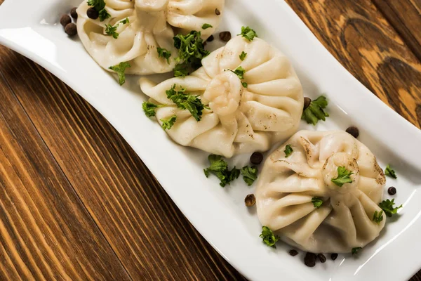 Nahaufnahme von köstlichem Chinkali mit Koriander auf Teller auf braunem Holztisch — Stockfoto