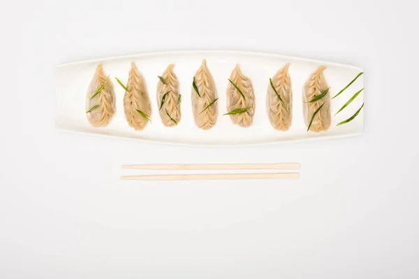 Вид на вкусные китайские вареные пельмени на тарелке рядом с палочками для еды на белом фоне — стоковое фото